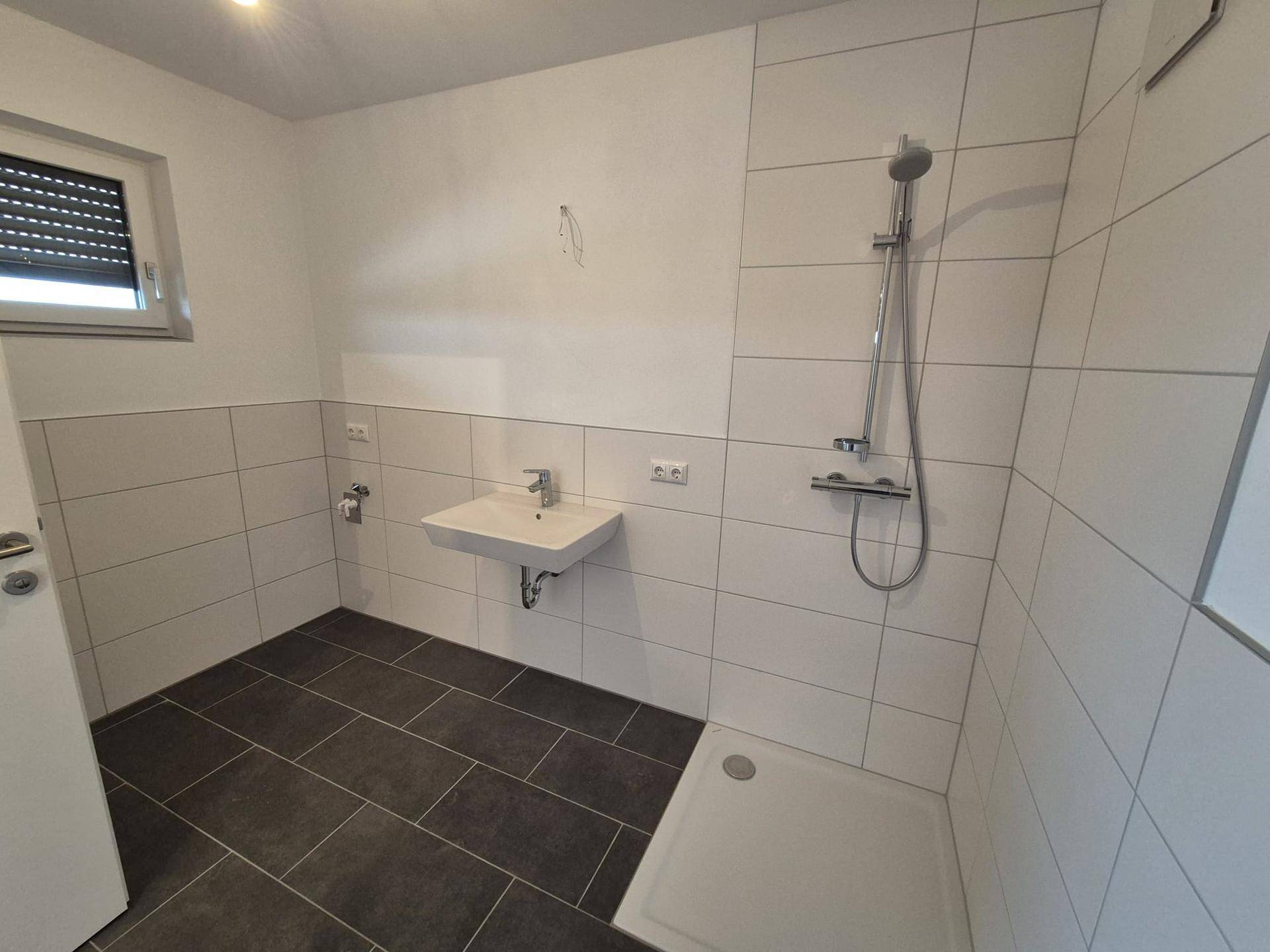 Helles Badezimmer mit Dusche, Waschbecken und einem Fenster für natürliche Belüftung.