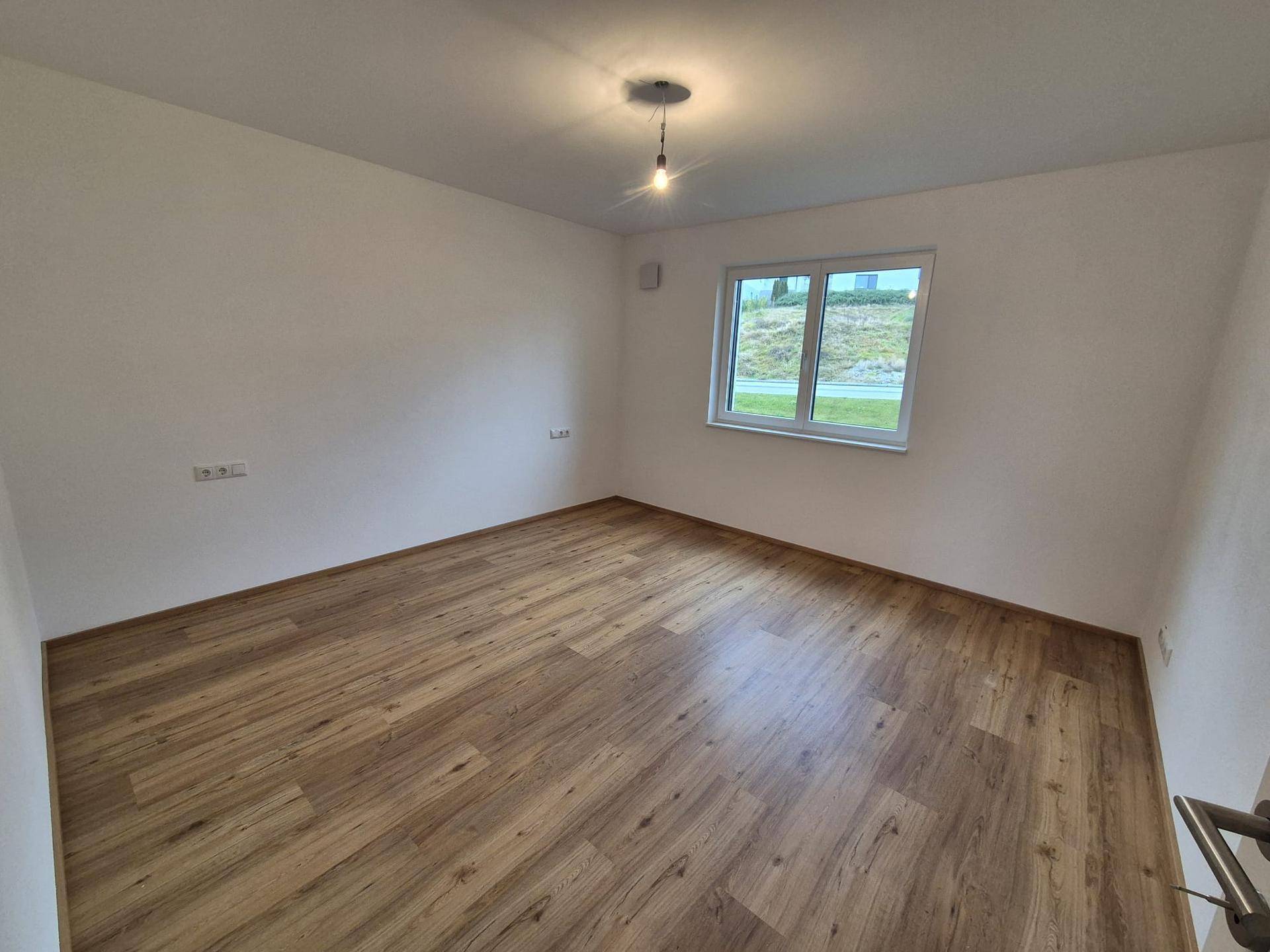 Helles Schlafzimmer mit Laminatboden und einem großen Fenster für natürliche Belichtung.