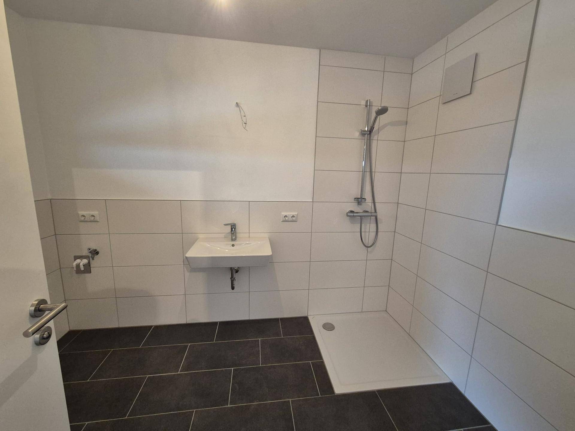 Modernes Badezimmer mit ebenerdiger Dusche, Waschbecken und hellen Wandfliesen.