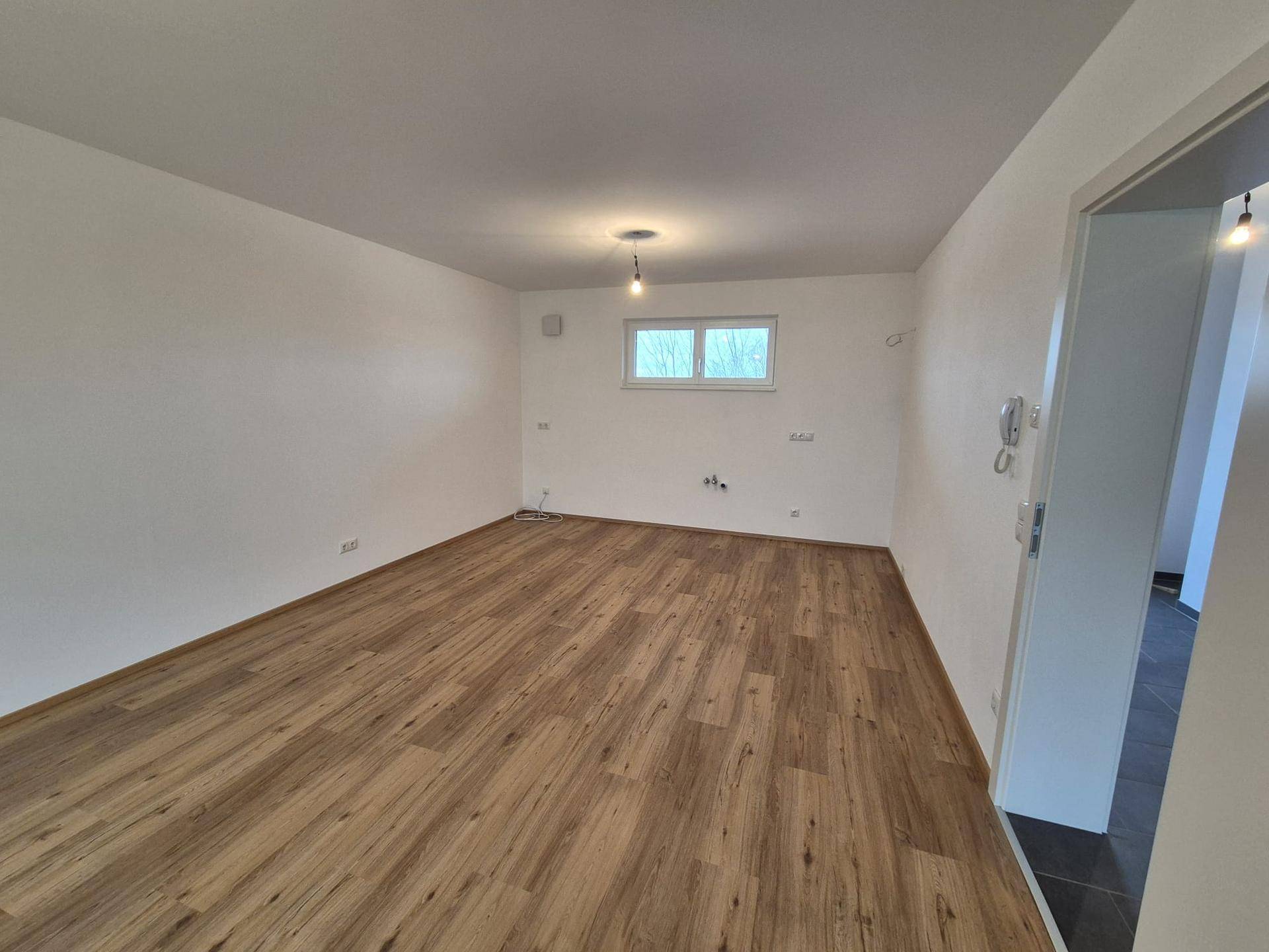 Geräumiges Wohnzimmer mit Laminatboden und einem Fenster, das viel Tageslicht hereinlässt.