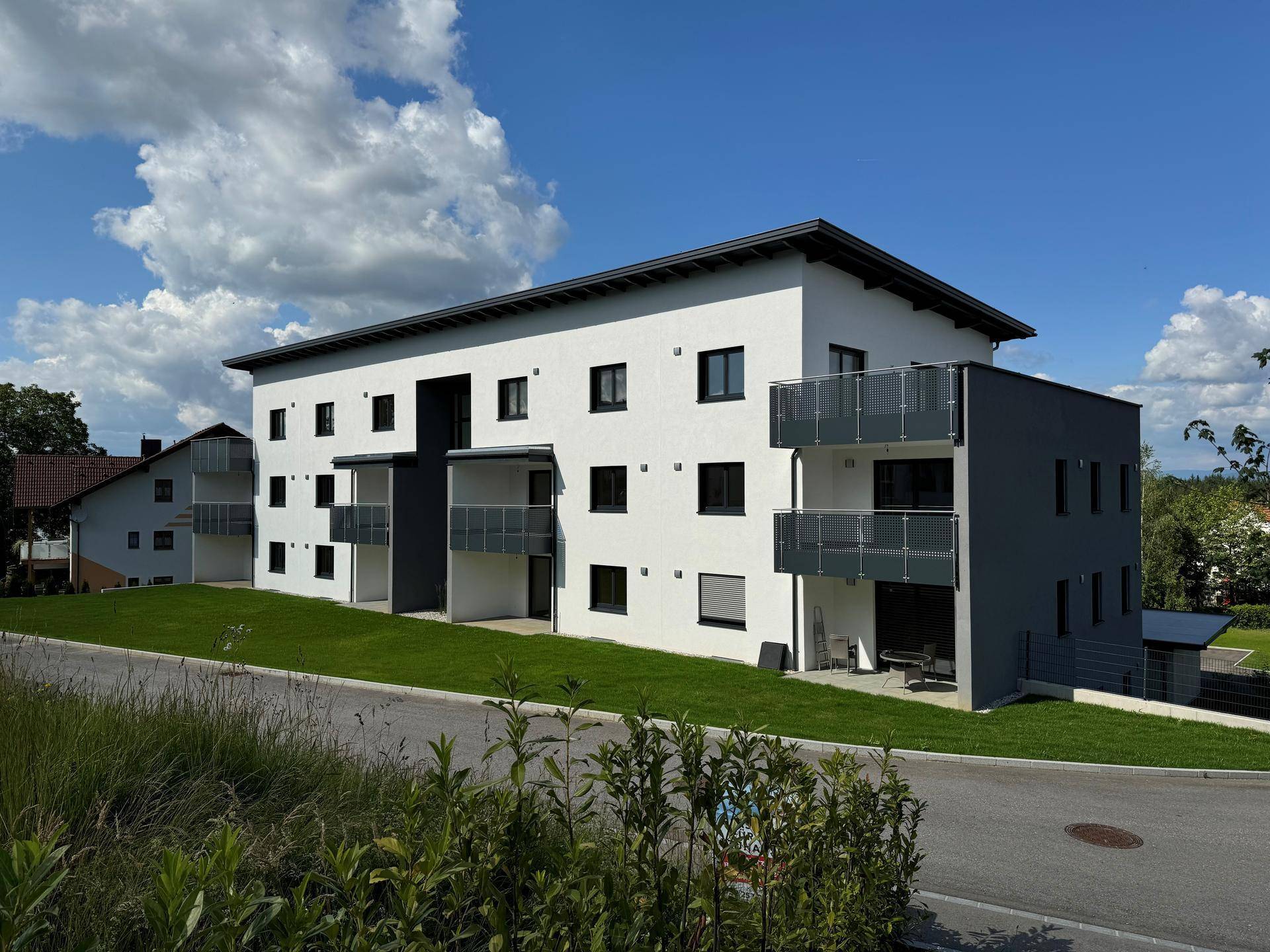 Modernes Wohngebäude mit weißer Fassade und Balkonen, eingebettet in eine grüne Hanglage.