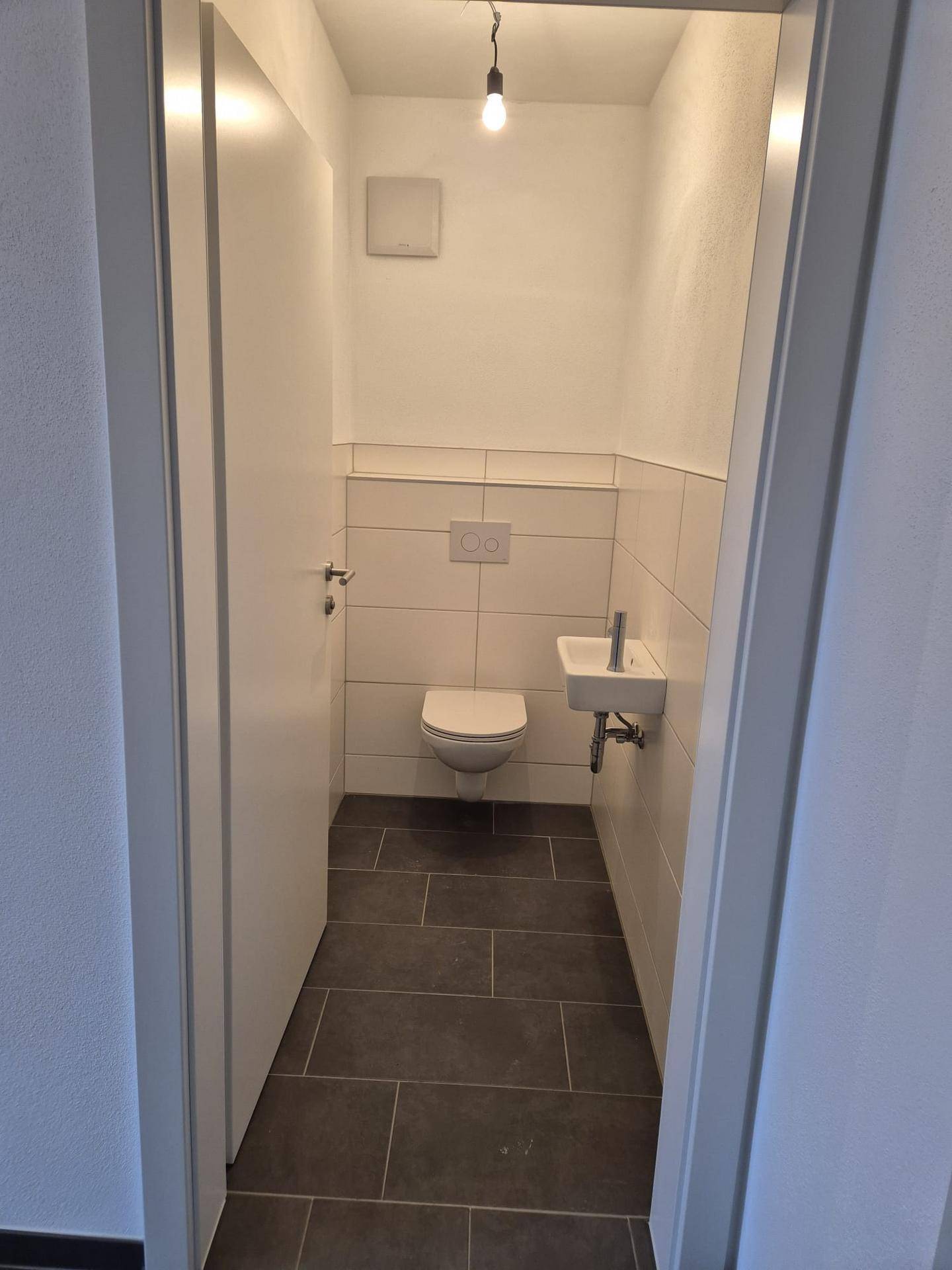 Modernes Gäste-WC mit wandhängender Toilette, kleinem Waschbecken und Fliesenboden.