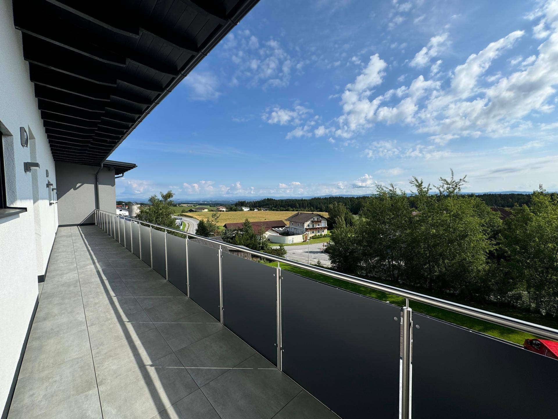 Geräumiger Balkon mit Fliesenboden und weitem Blick über die grüne Landschaft.
