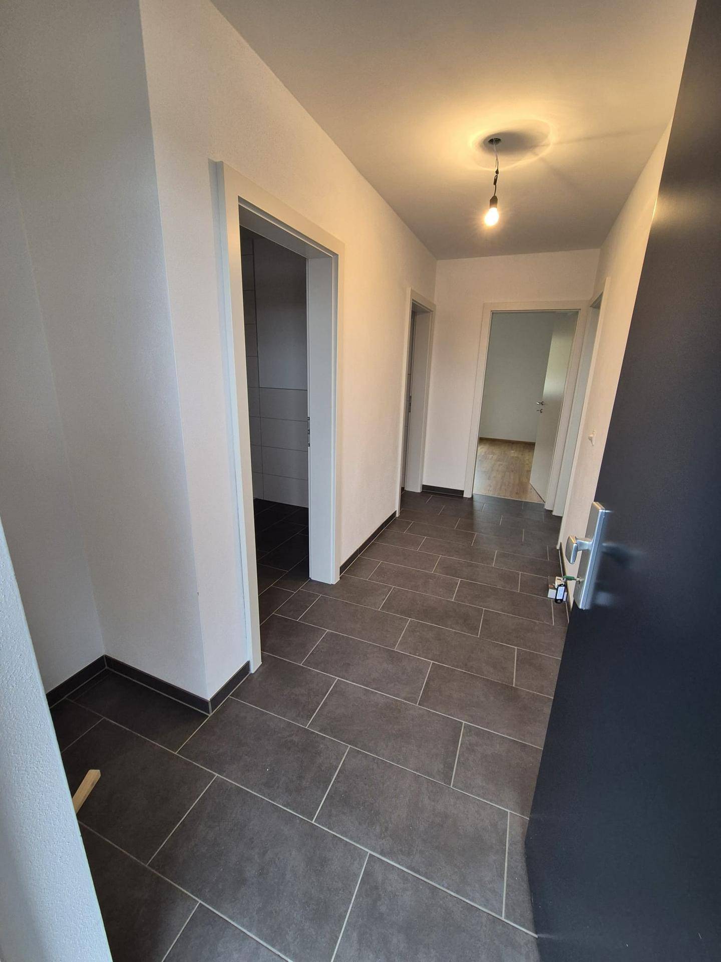 Moderner Flur mit dunklen Fliesen und Zugang zu verschiedenen Räumen der Wohnung.