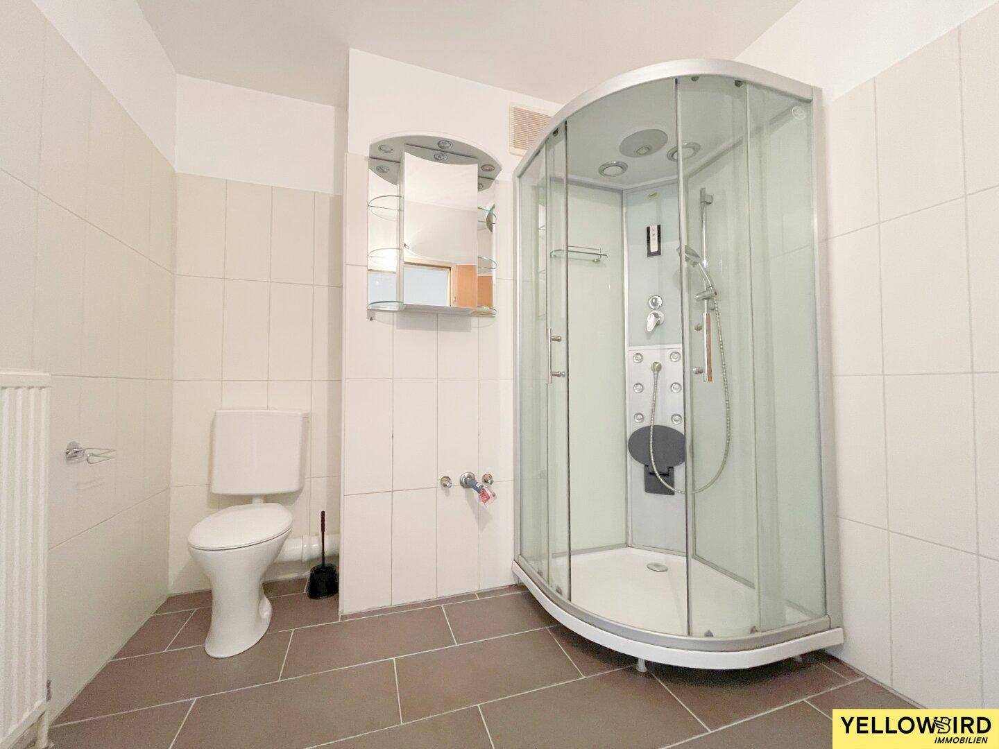 Badezimmer mit Duschkabine, Toilette und hellen Fliesen an Wänden und Boden.