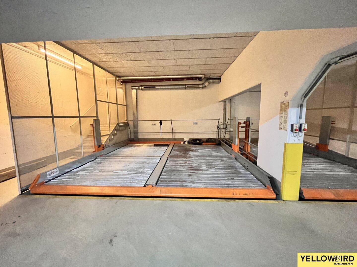 Geräumige Tiefgarage mit zwei Doppelparker-Systemen und Zugang über eine Treppe im Hintergrund.