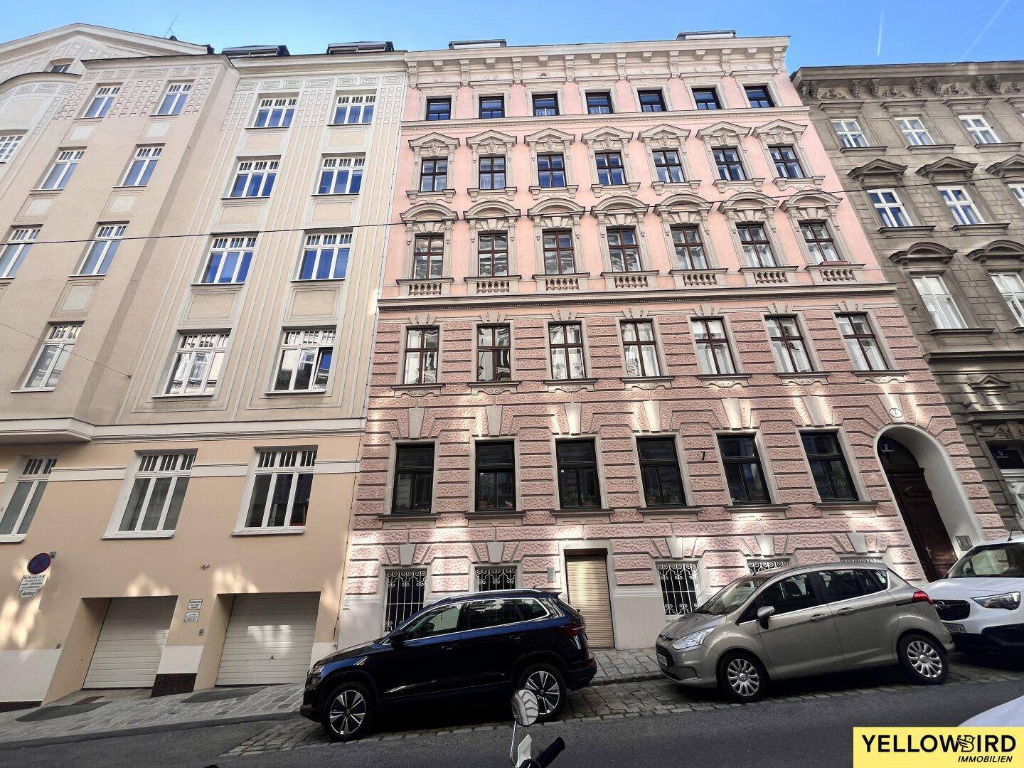 Historisches Wohngebäude mit rosa Fassade und vielen Fenstern in einer städtischen Umgebung.