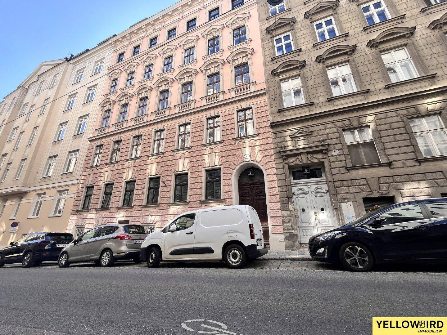 Historisches Wohngebäude mit rosa Fassade und vielen Fenstern in einer städtischen Umgebung.