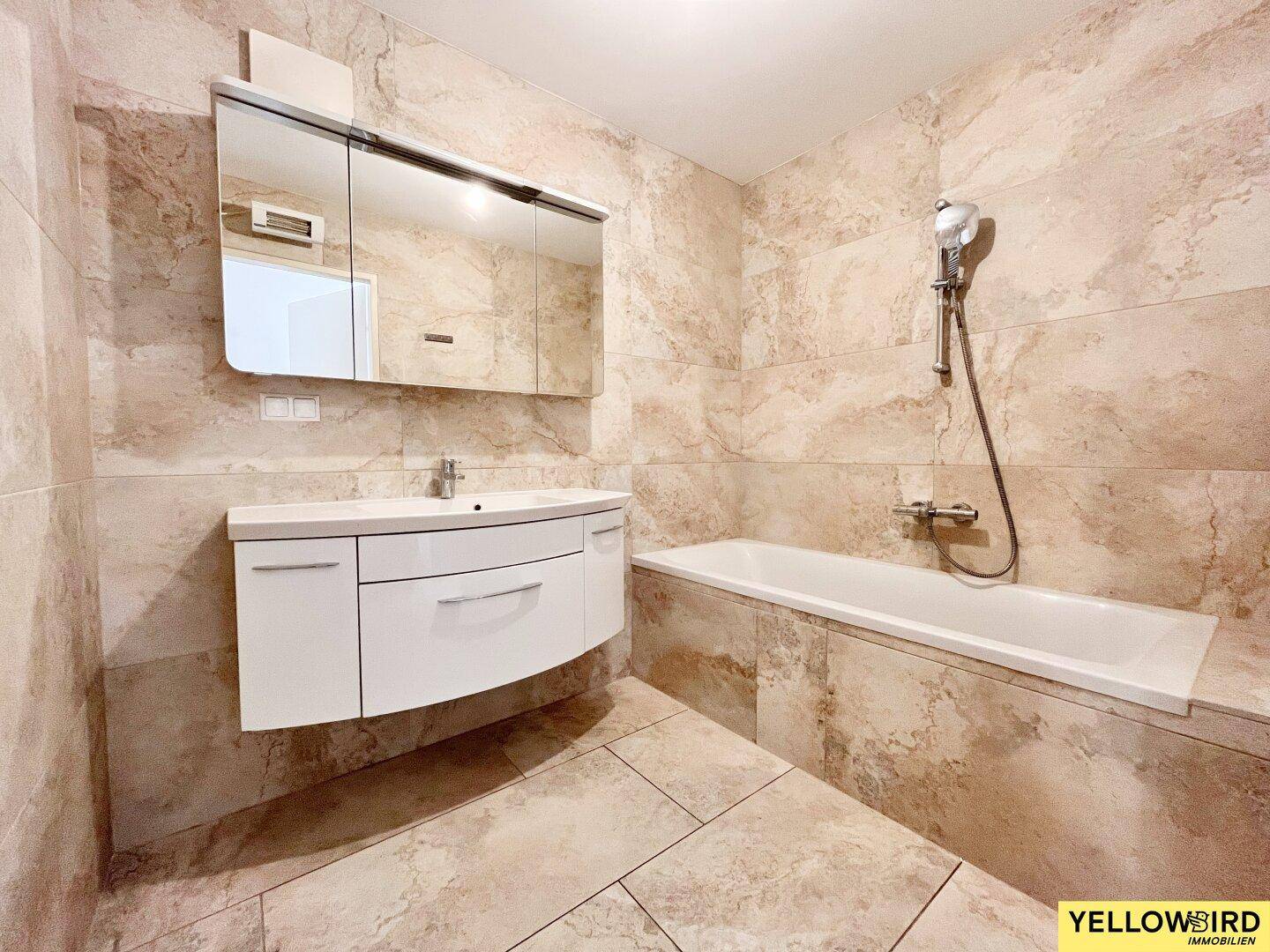 Modernes Badezimmer mit beigefarbenen Fliesen, Badewanne und Waschtisch mit Spiegelschrank.
