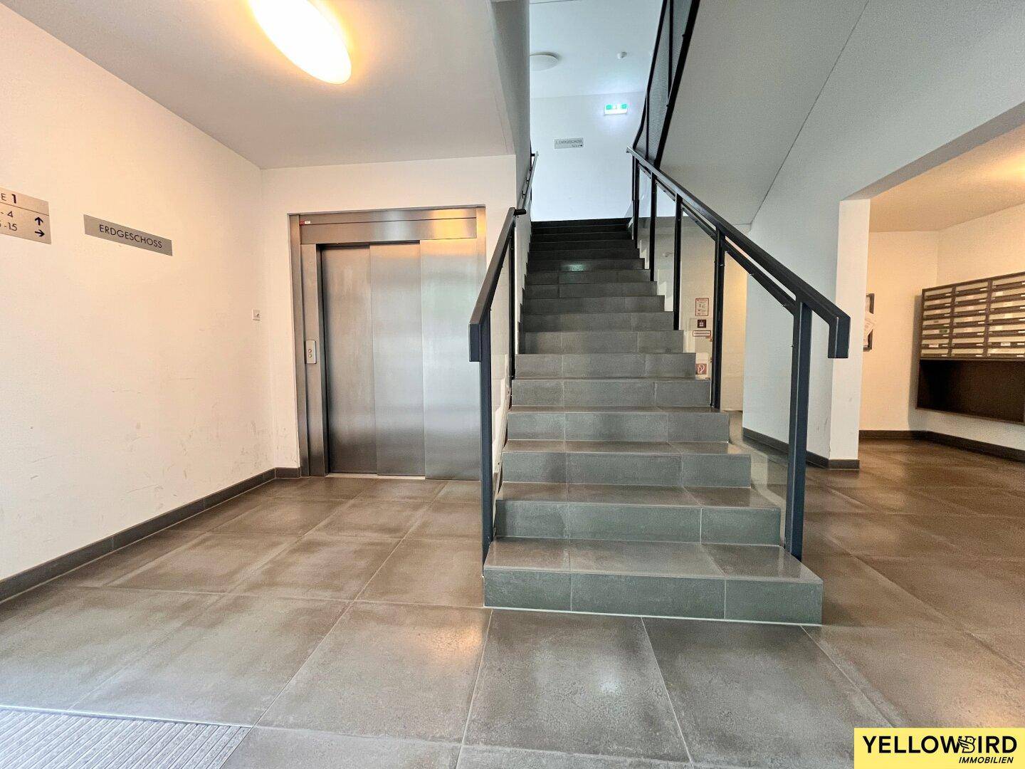 Eingangsbereich mit Treppenhaus und Aufzug, der Zugang zu den verschiedenen Etagen bietet.
