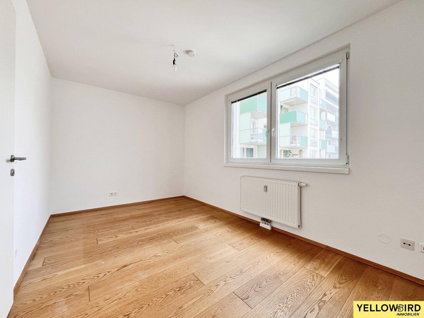 Geräumiges Schlafzimmer mit Parkettboden und großem Fenster, das viel natürliches Licht hereinlässt.