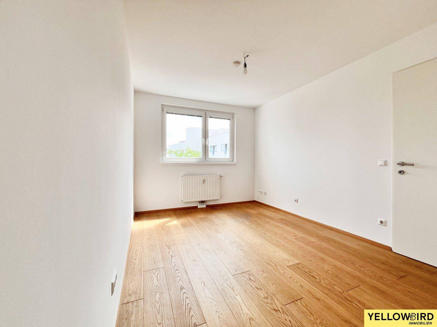Freundliches Schlafzimmer mit hellem Parkettboden und einem großen Fenster für viel Tageslicht.