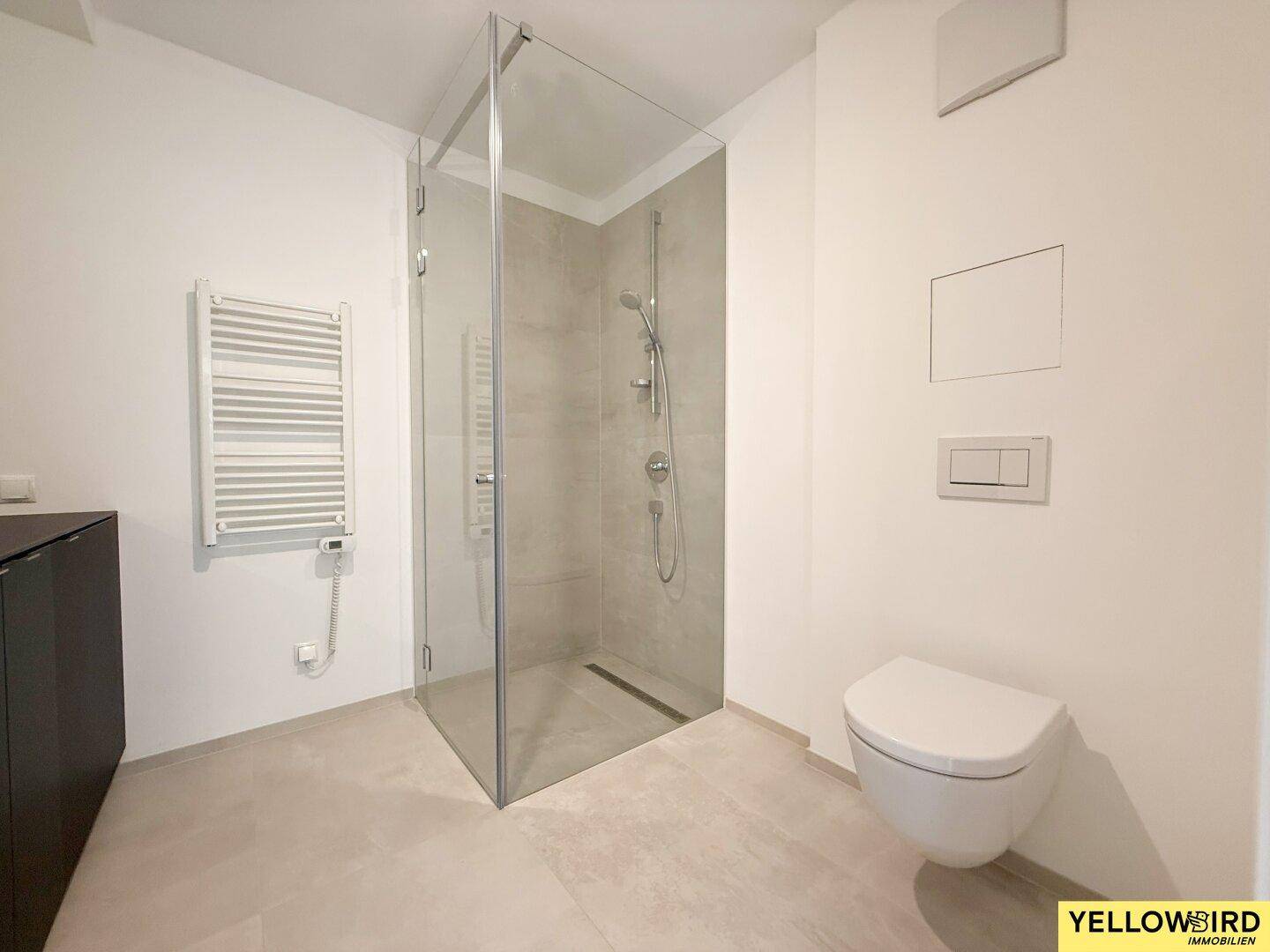 Helles Badezimmer mit ebenerdiger Glasdusche, wandhängendem WC und modernem Handtuchheizkörper.