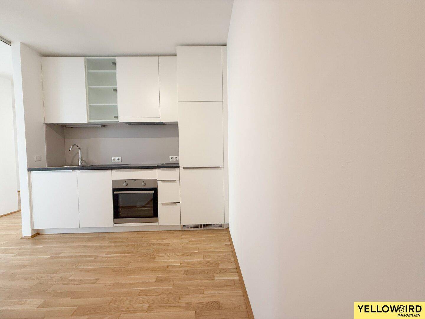 Moderne Einbauküche mit weißen Schränken, dunkler Arbeitsplatte und integriertem Backofen.