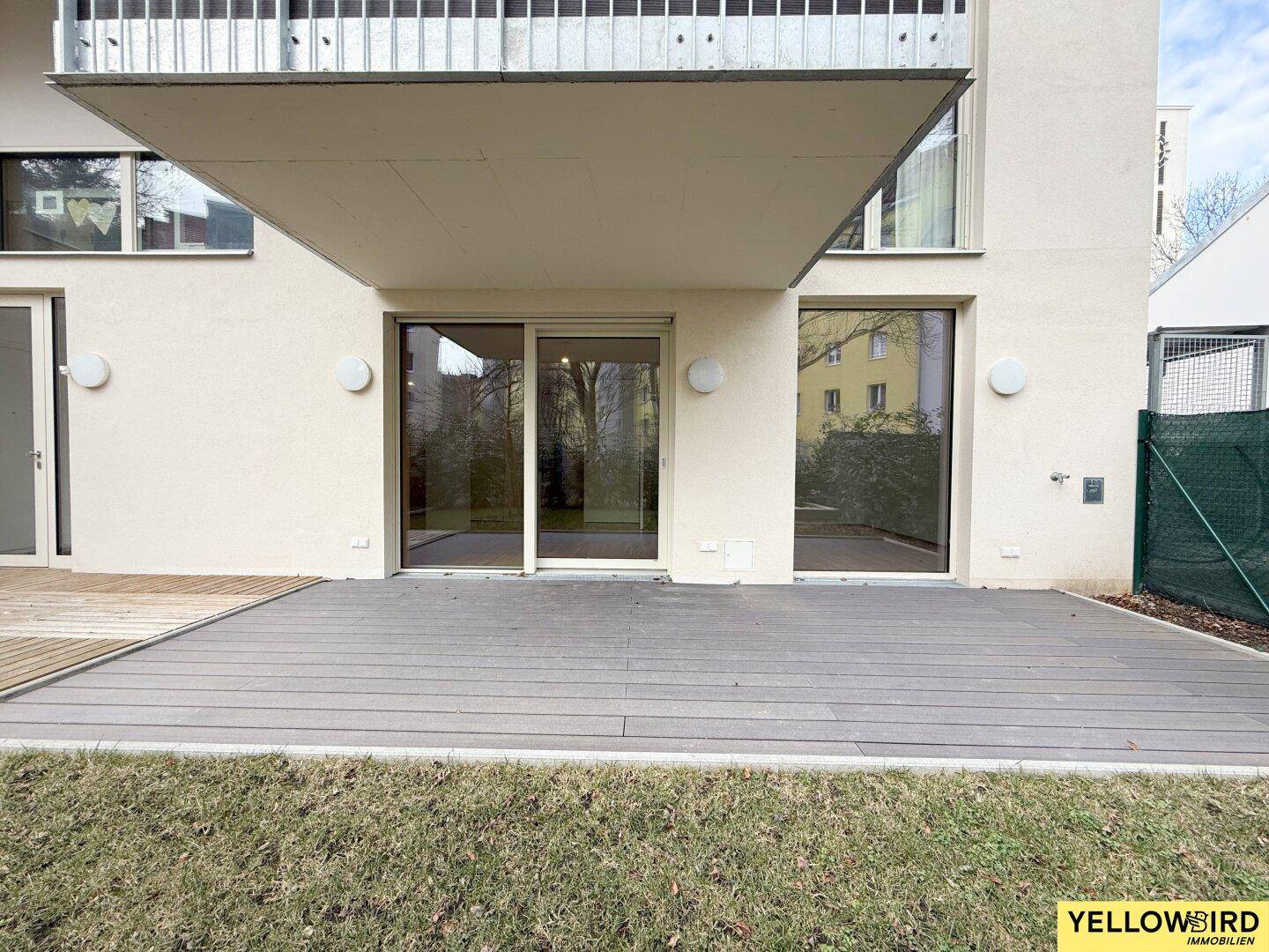 Außenansicht des Gebäudes mit einer großen Holzterrasse und angrenzender Rasenfläche.