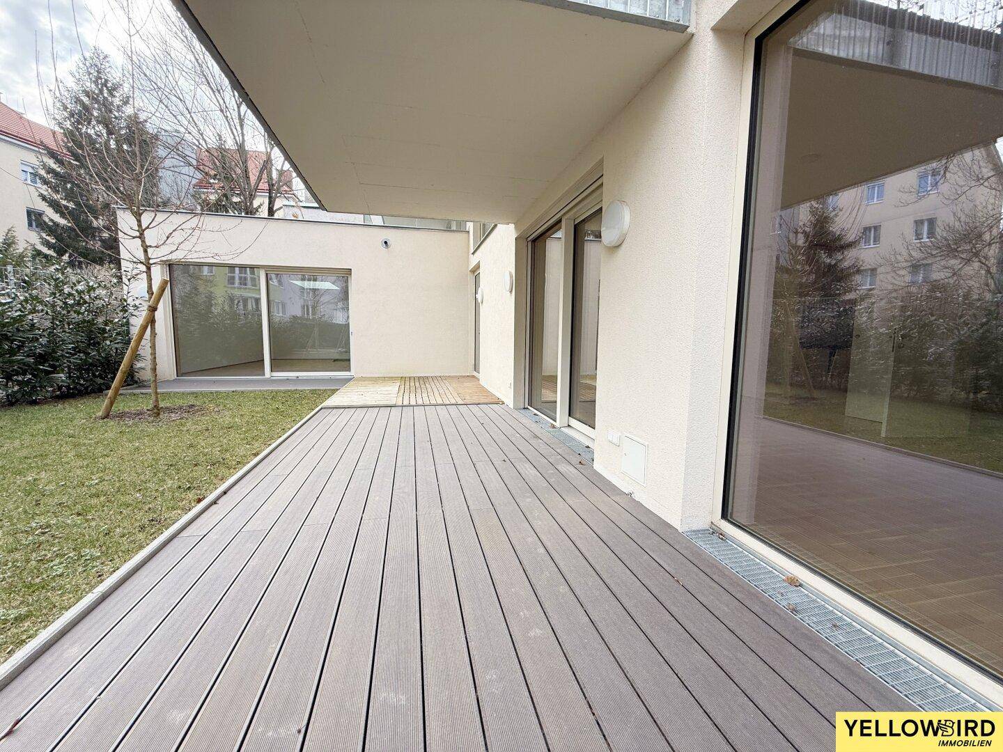 Weitläufige Holzterrasse am Gebäude mit Blick auf die umliegende Grünfläche.