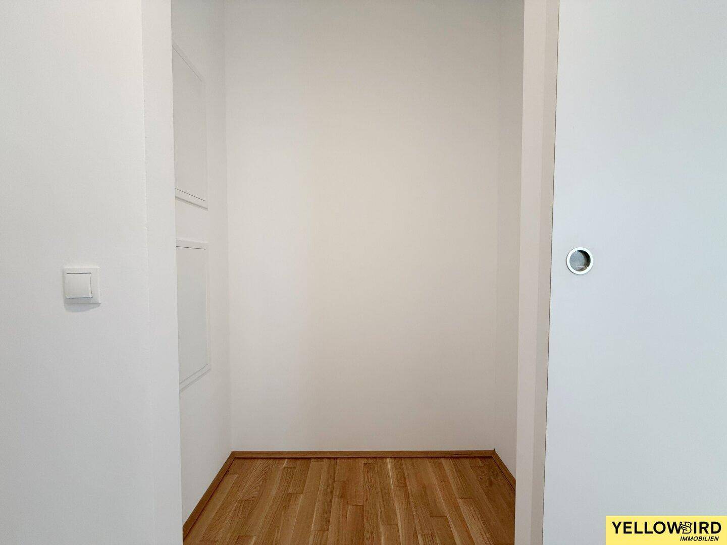 Kleiner, leerer Abstellraum oder begehbarer Schrank mit hellem Holzboden und weißen Wänden.