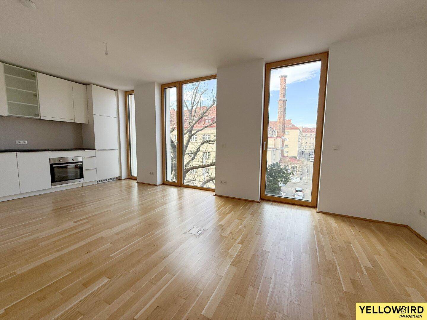 Heller Wohnbereich mit offener Küche und großen Fenstern, die einen urbanen Ausblick auf die Stadt bieten.
