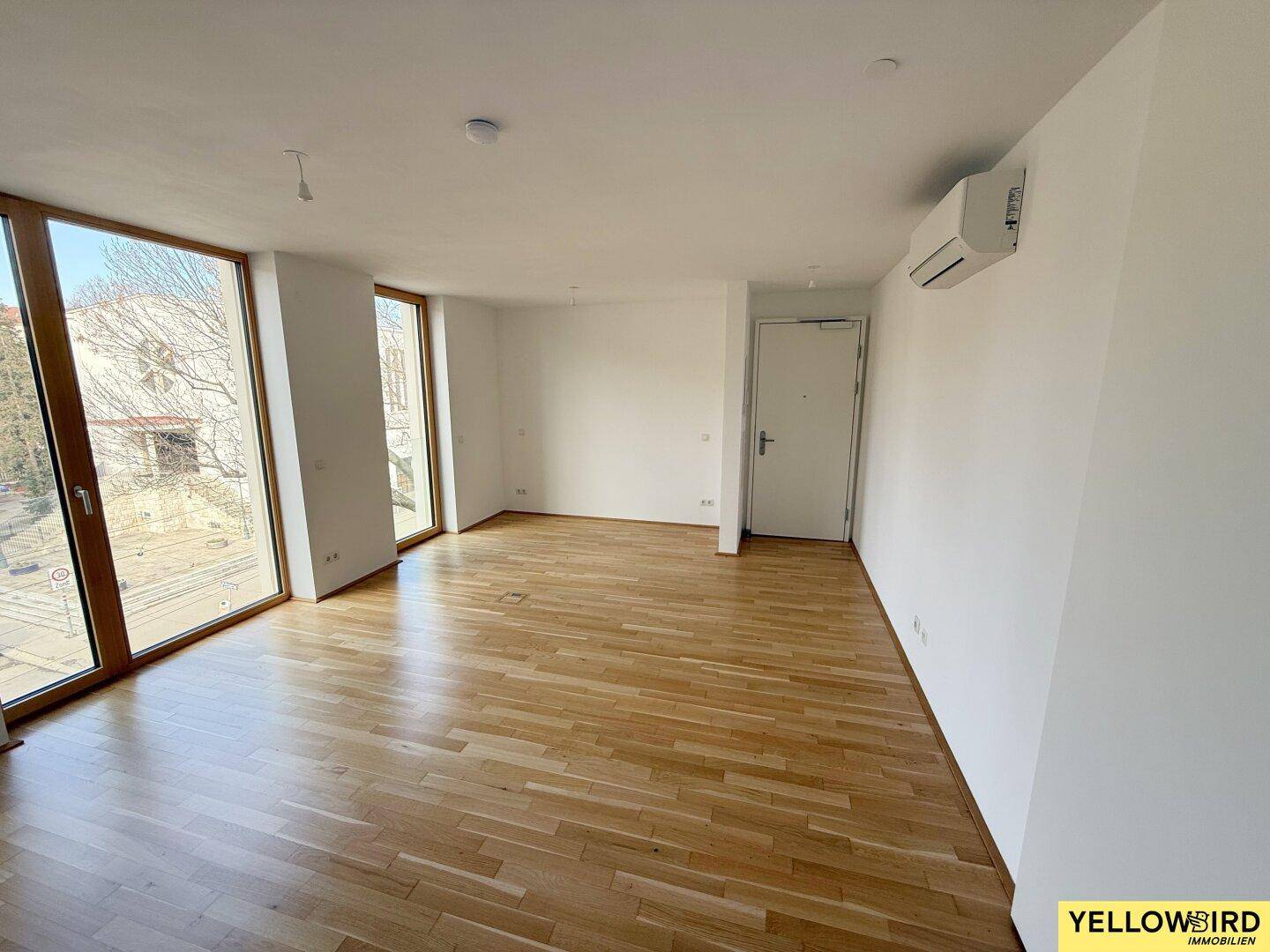 Heller Eingangsbereich mit großen Fenstern und Holzboden, der viel Tageslicht in den Raum lässt.