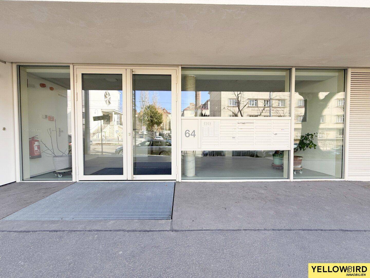 Gebäudeeingang mit einer Rampe für Barrierefreiheit und durch die Glasfront sichtbaren Briefkästen.