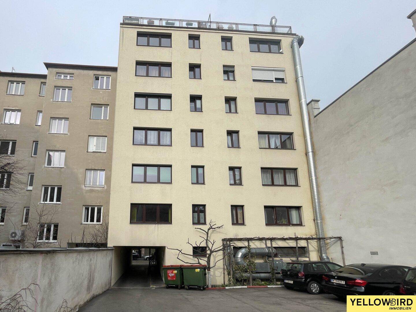 Seitenansicht des Gebäudes mit Zufahrt und Parkplätzen im Hinterhofbereich.