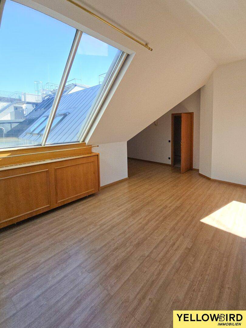 Heller Dachgeschossraum mit schrägem Dach, Laminatboden und einem großen Dachfenster, das den Raum erhellt.