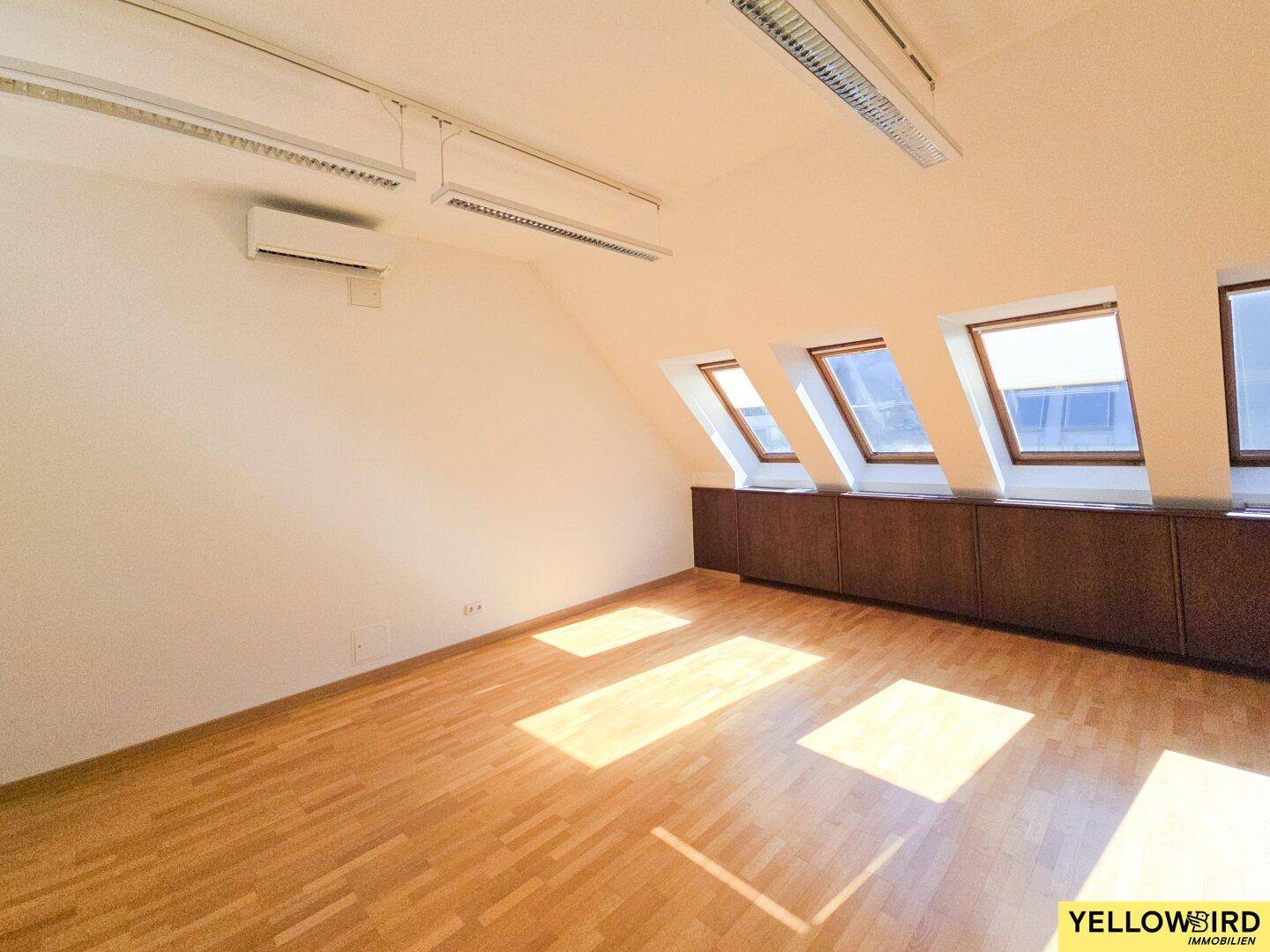 Dachgeschossraum mit schrägem Dach, Parkettboden, Dachfenstern und einer Klimaanlage an der Wand.