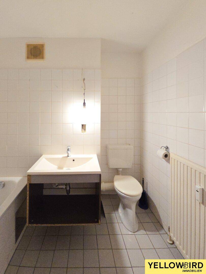 Badezimmer mit weißen Fliesen, Toilette, Waschbecken und Heizkörper, renovierungsbedürftig.