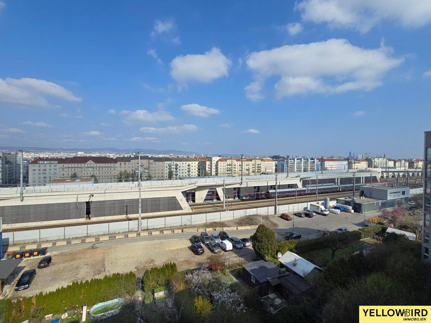 Weitblick über die Stadt mit Bahngleisen und umliegenden Gebäuden unter blauem Himmel.