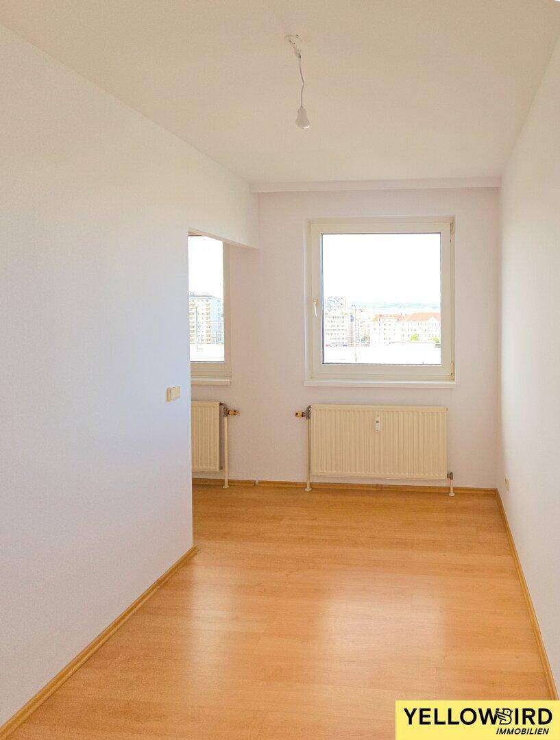 Heller Raum mit Parkettboden, zwei Fenstern und Heizkörpern, bietet Weitblick.
