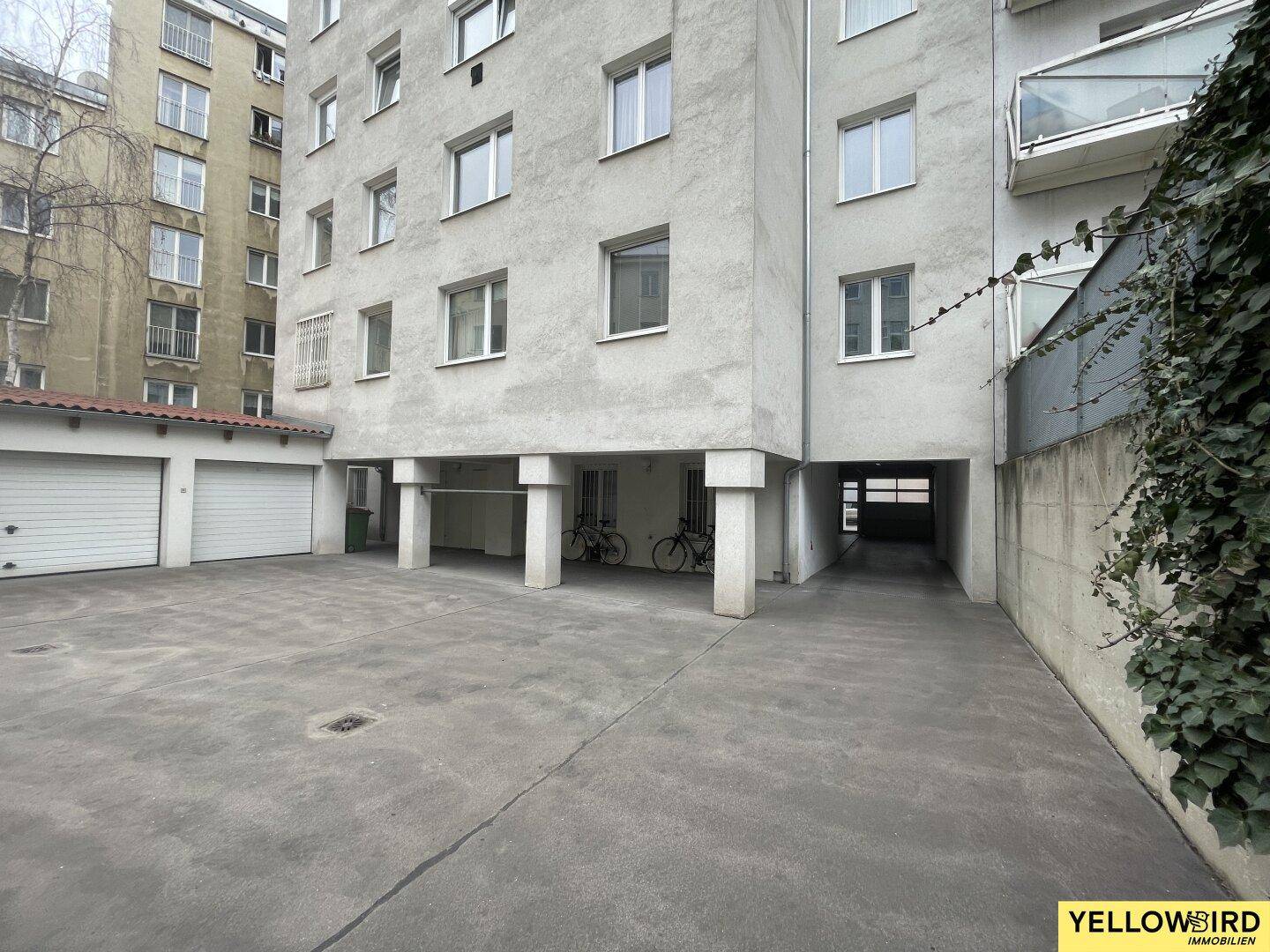 Hinterhofbereich mit Parkplätzen, Garagen und einem Durchgang unter dem Gebäude.