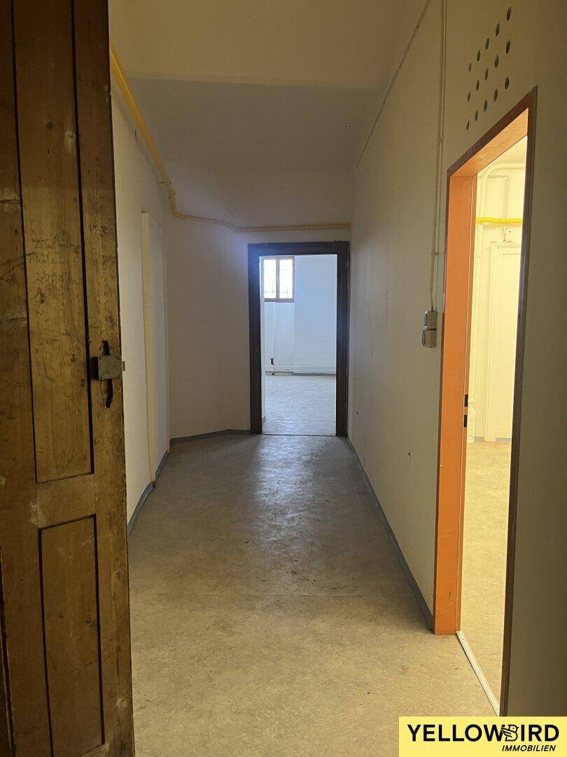 Langer, leerer Flur mit Betonboden und weißen Wänden, der zu weiteren Räumen führt.