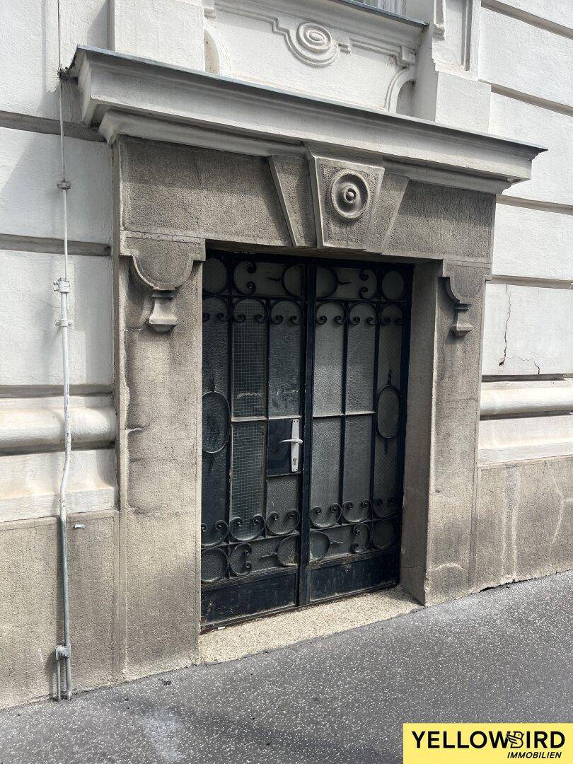 Einfacher, historischer Eingang mit schmiedeeisernem Gittertor und robustem Steinfensterrahmen.