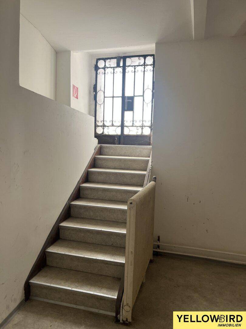 Schlichtes Treppenhaus mit Steinstufen und einem Metallgittertor am oberen Ende.