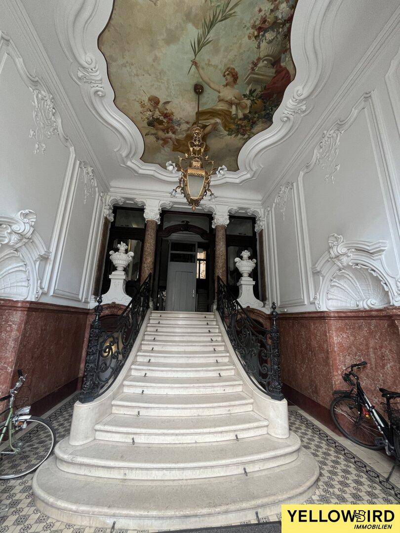 Prächtiger Eingangsbereich mit einer geschwungenen Steintreppe, kunstvoller Deckenmalerei und Stuckverzierungen.