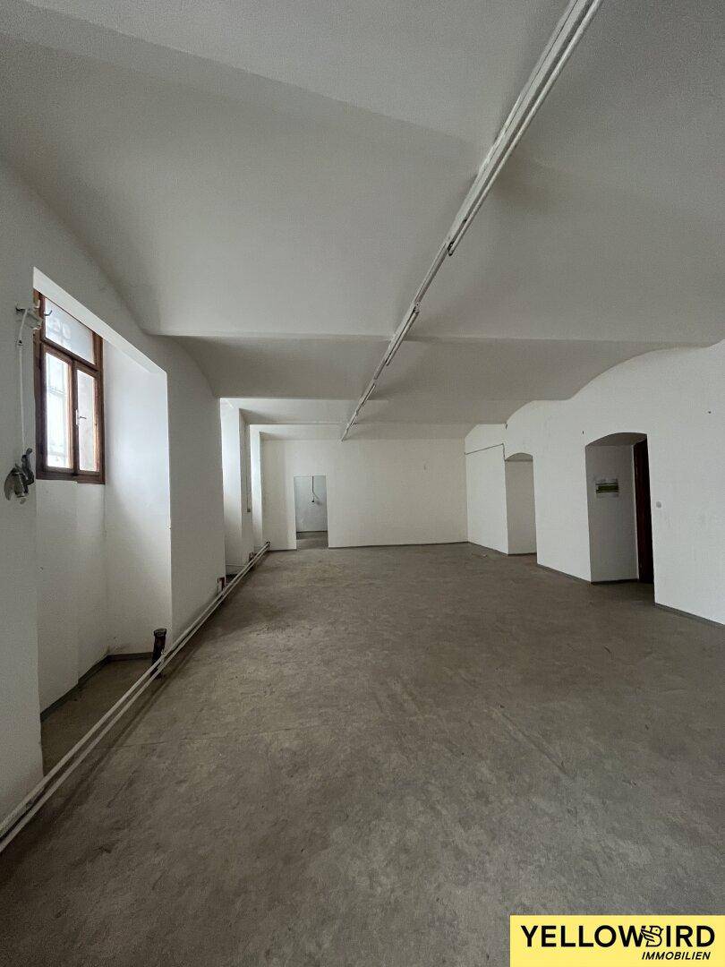 Geräumiger, leerer Raum mit Betonboden, weißen Wänden und Fenstern, geeignet für gewerbliche Nutzung.