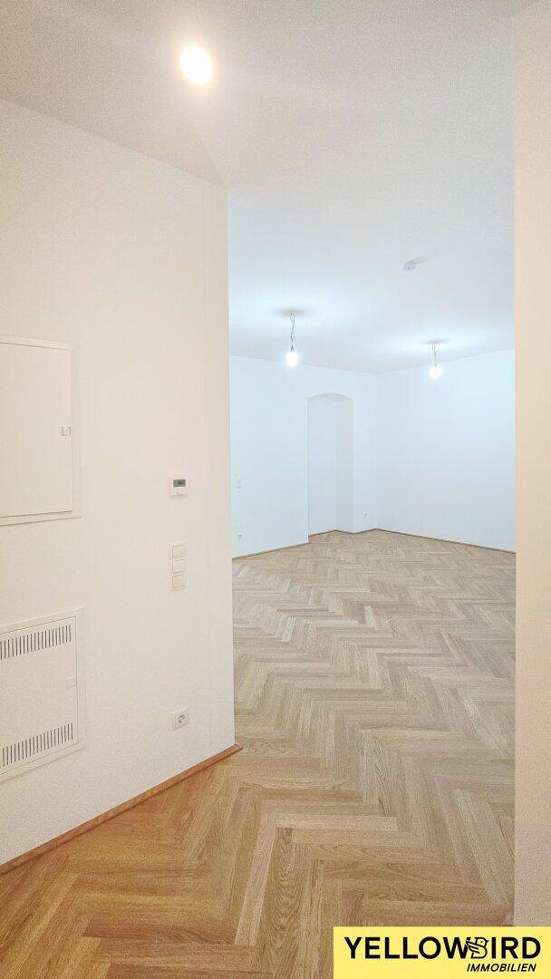 Heller Flur mit Fischgrätparkettboden, der zu weiteren leeren Räumen der Wohnung führt.
