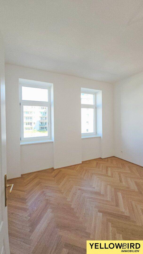 Geräumiges, helles Schlafzimmer mit Fischgrätparkett und zwei großen Fenstern.