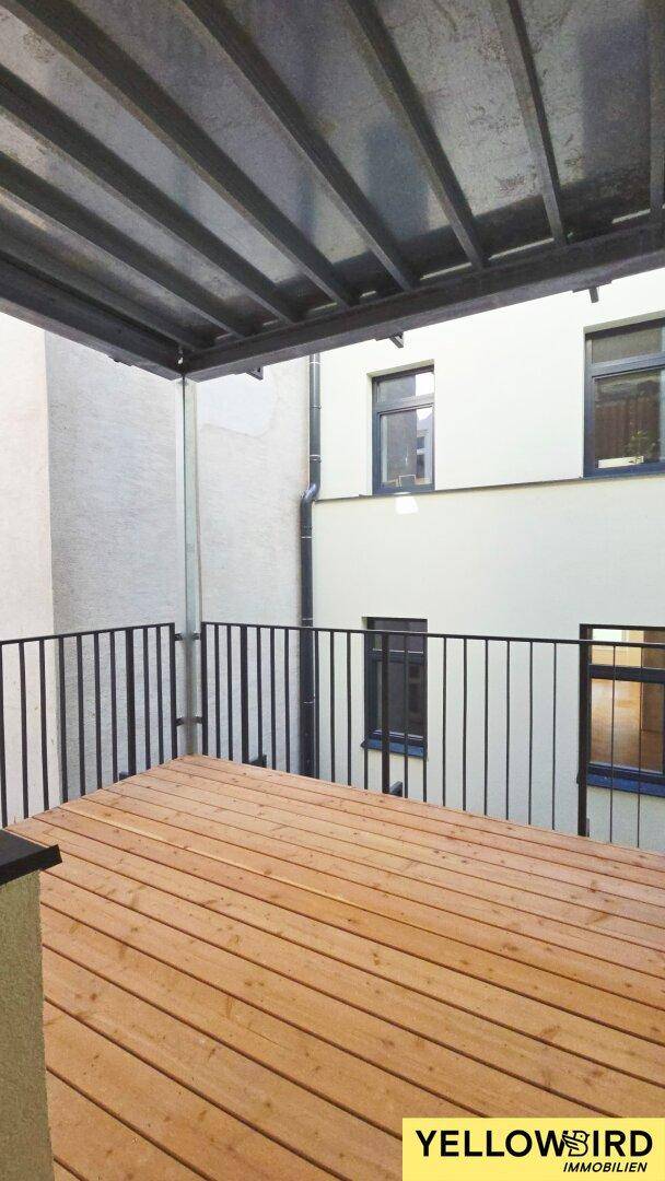 Geräumige Holzterrasse mit schwarzem Geländer und Überdachung, ideal für entspannte Stunden im Freien.