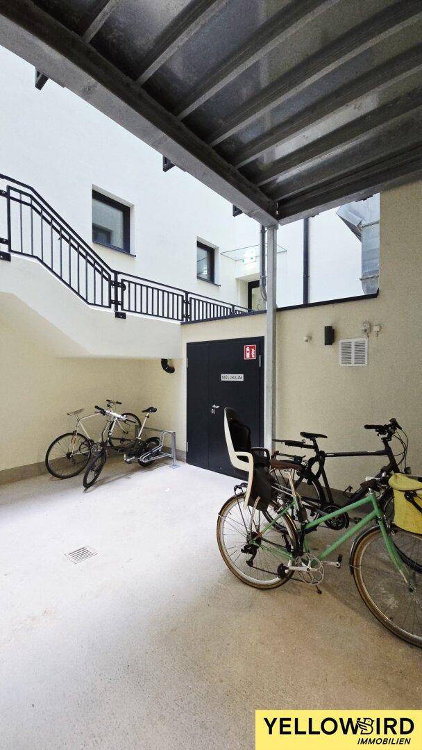 Überdachter Fahrradabstellplatz im Freien mit mehreren Fahrrädern und Zugangstür.