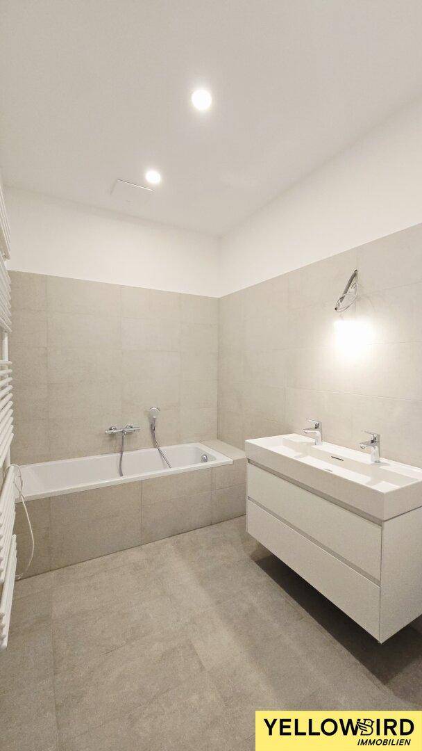 Modernes Badezimmer mit Badewanne, Doppelwaschbecken und großformatigen Fliesen.