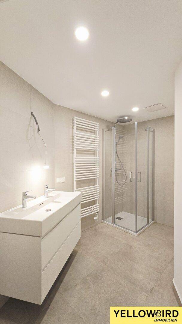 Modernes Badezimmer mit Doppelwaschbecken, Duschkabine und beheiztem Handtuchhalter.
