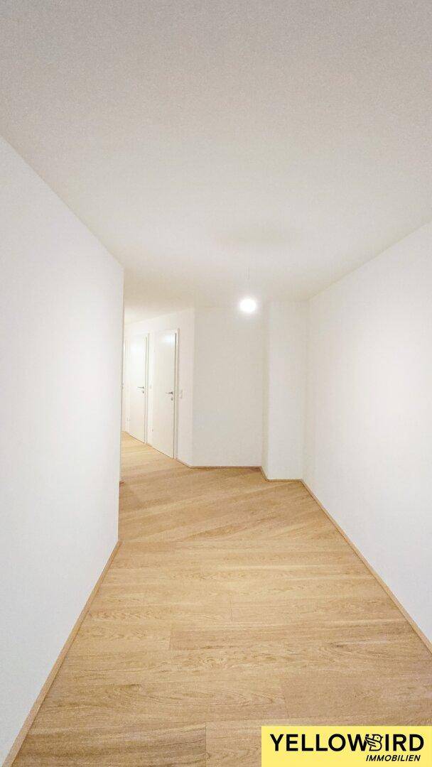 Heller Flur mit Holzboden und weißen Wänden, der zu weiteren Räumen führt.