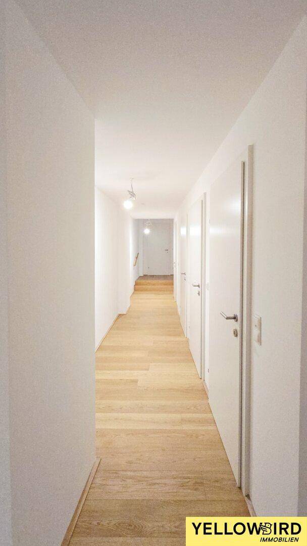 Langer, heller Flur mit Holzboden und mehreren Türen, der die Zimmer verbindet.