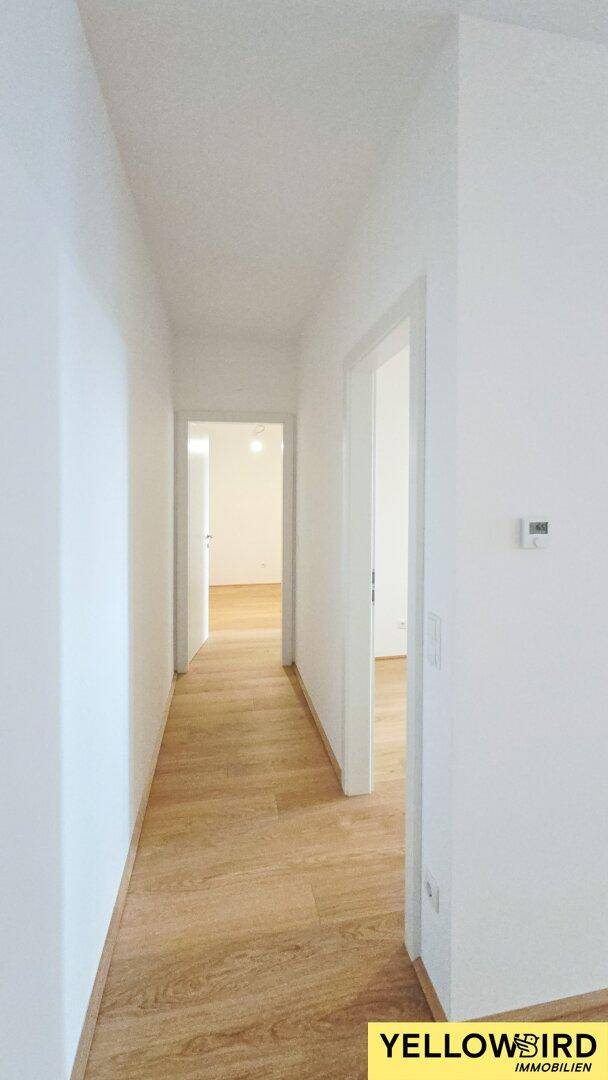 Heller Flur mit Holzboden und weißen Wänden, der zu verschiedenen Zimmern führt.