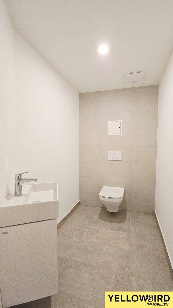 Helles Gäste-WC mit modernen Fliesen, wandhängender Toilette und Waschbecken.