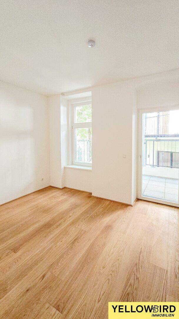 Helles Zimmer mit Holzboden und Zugang zu einem Außenbereich, ideal als Schlafzimmer.