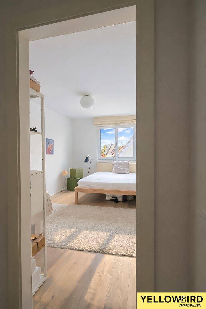Helles Schlafzimmer mit Holzboden und Fenster, das einen Blick auf den Himmel und die Dächer bietet.