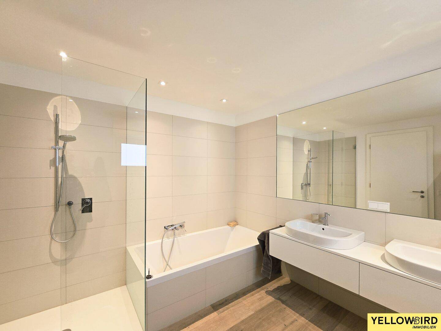 Modernes Badezimmer mit Badewanne, begehbarer Dusche und Doppelwaschbecken, hell gefliest.