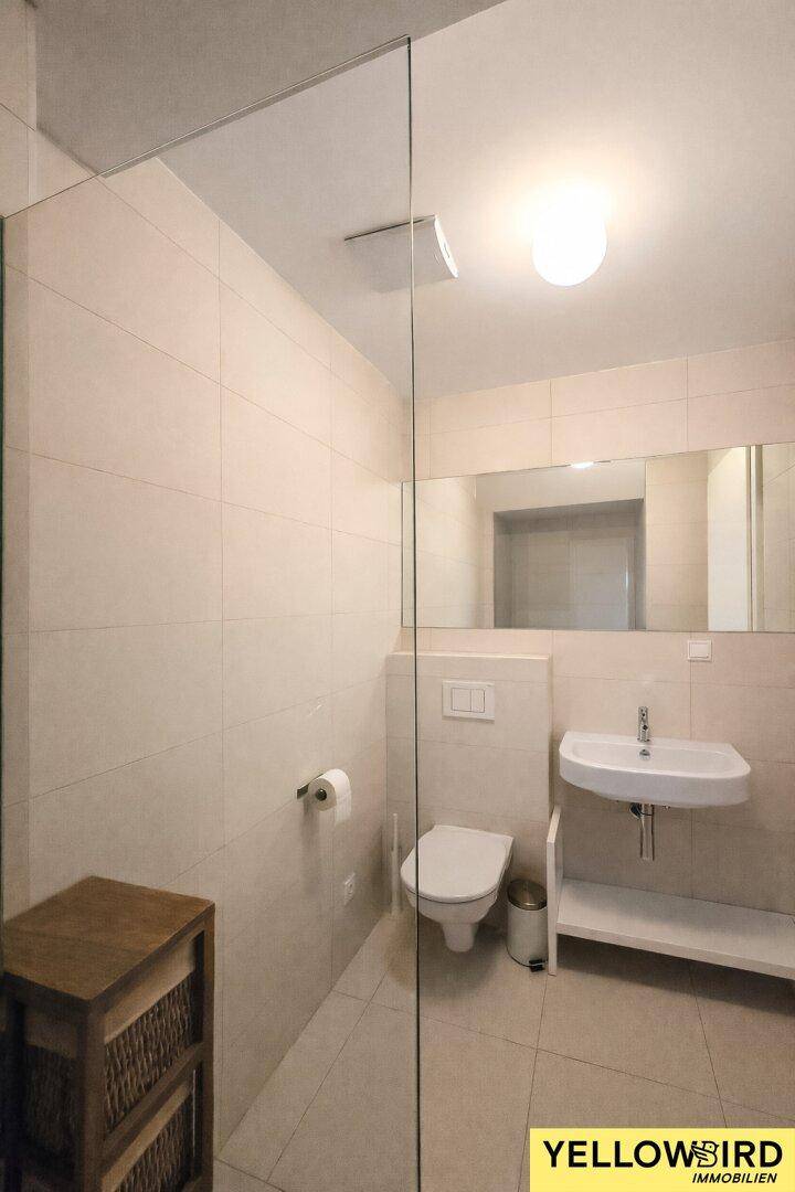 Modernes Gäste-WC mit Dusche, Wand-WC und Waschbecken, hell gefliest.